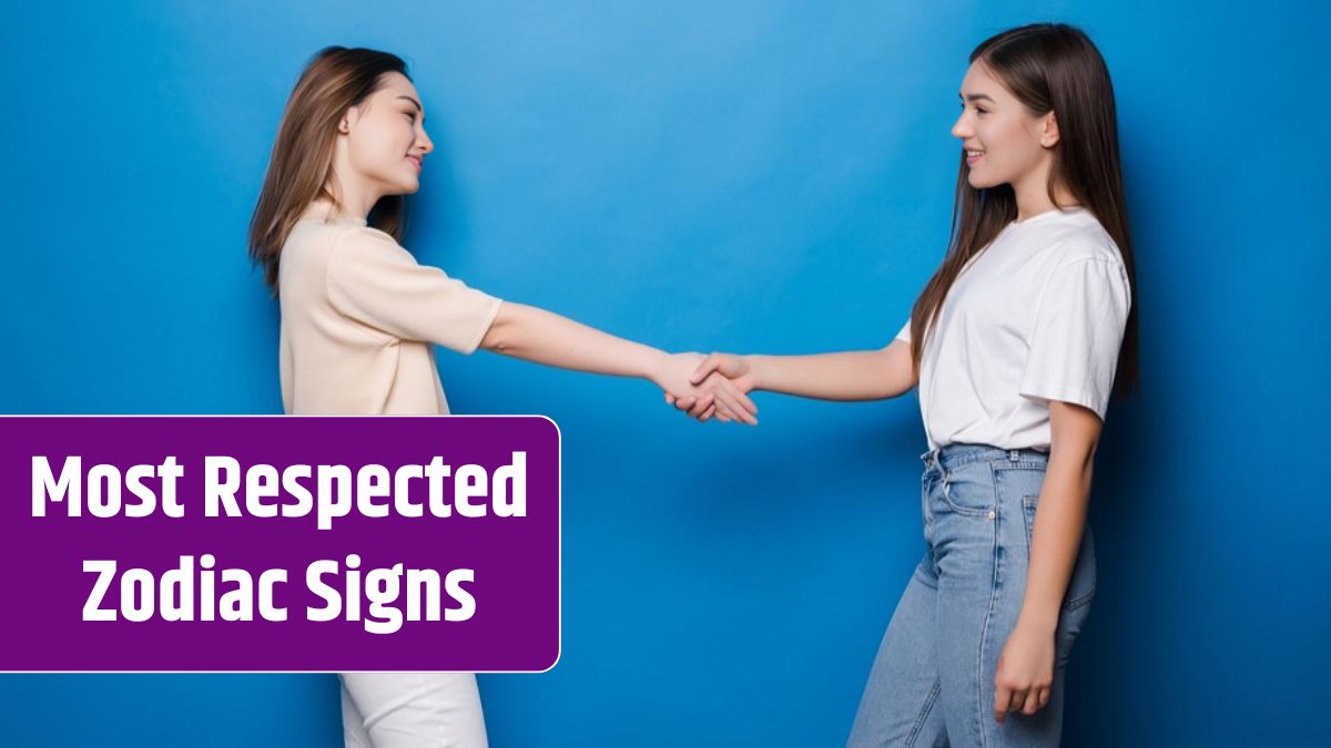 Two young women, standing and dressed casually, shaking hands and smiling on blue wall.